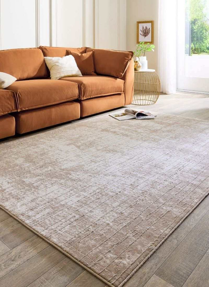 Abstract geometric rug in neutral tones of beige and grey, placed under a cozy orange sofa with soft pillows.