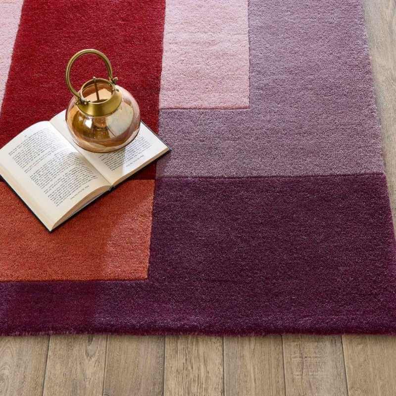 Hand-carved multicoloured geometric wool rug with a book and decorative pot on wooden floor.