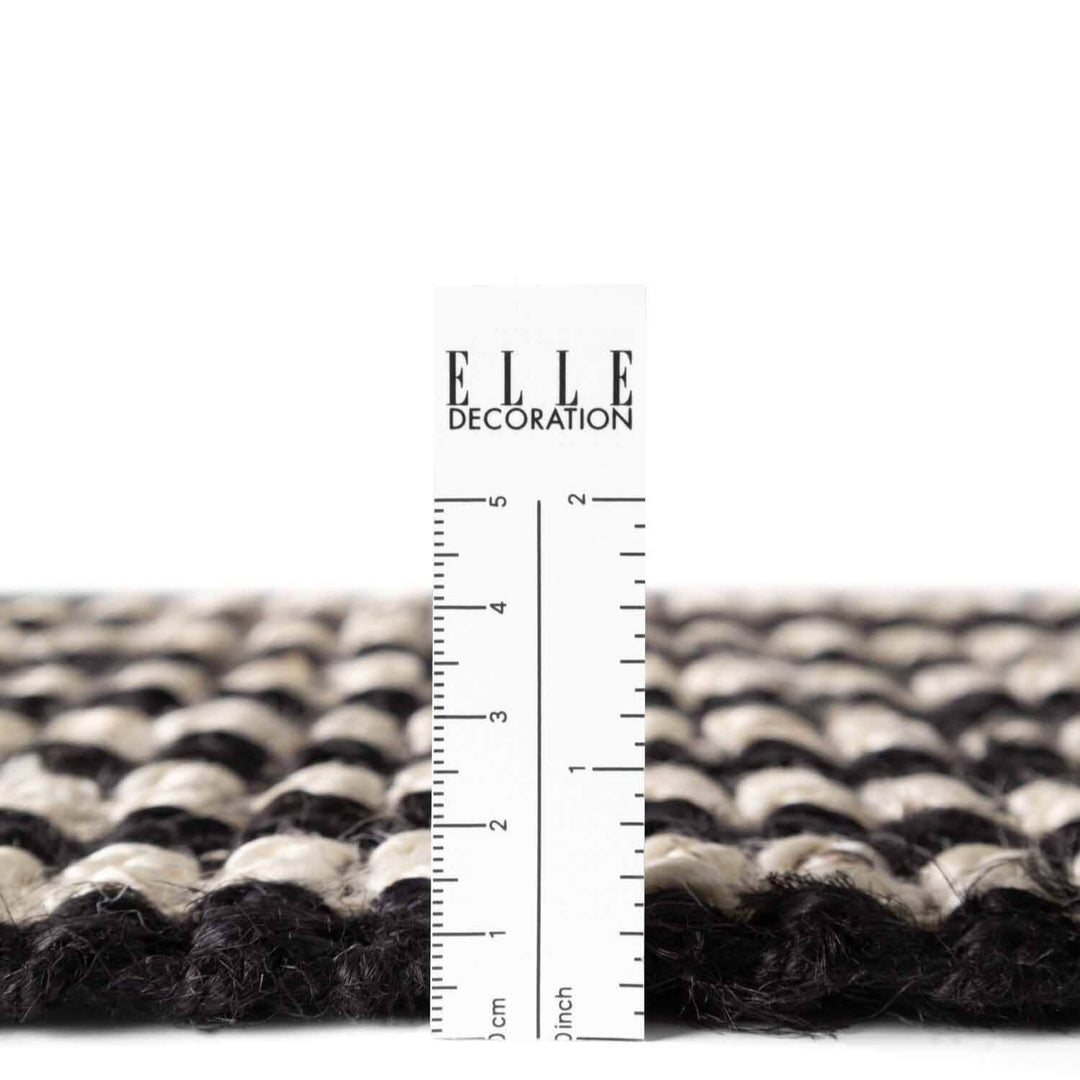 Textured black and white rug with a ruler for scale on a white background, featuring the 'ELLE Decoration' brand.
