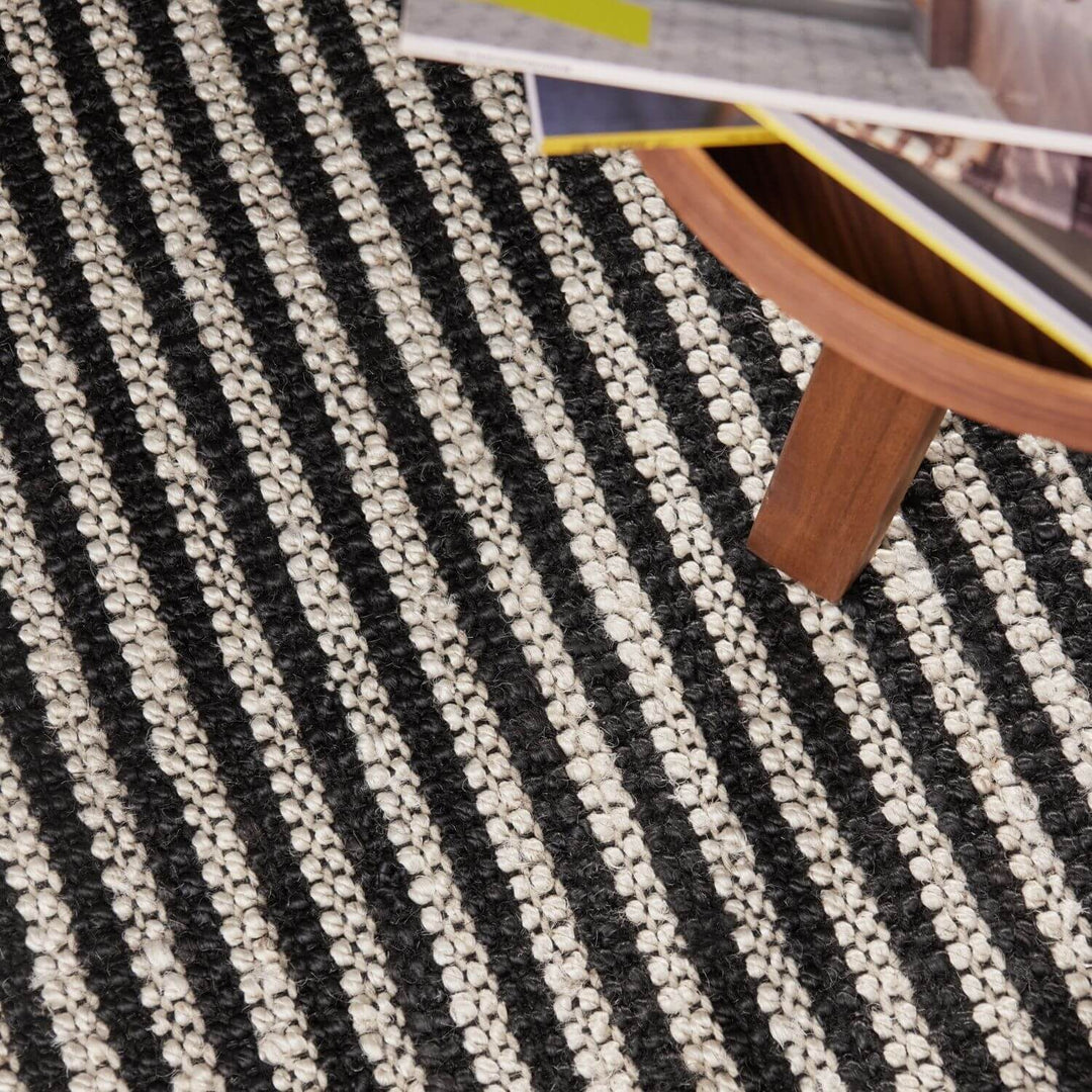 Close-up of a black and white striped rug with a wooden chair leg partially visible.