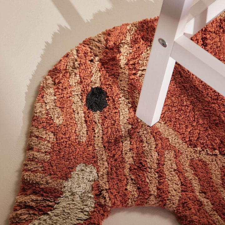 Textured red and beige rug with a white chair leg on a light-colored floor.