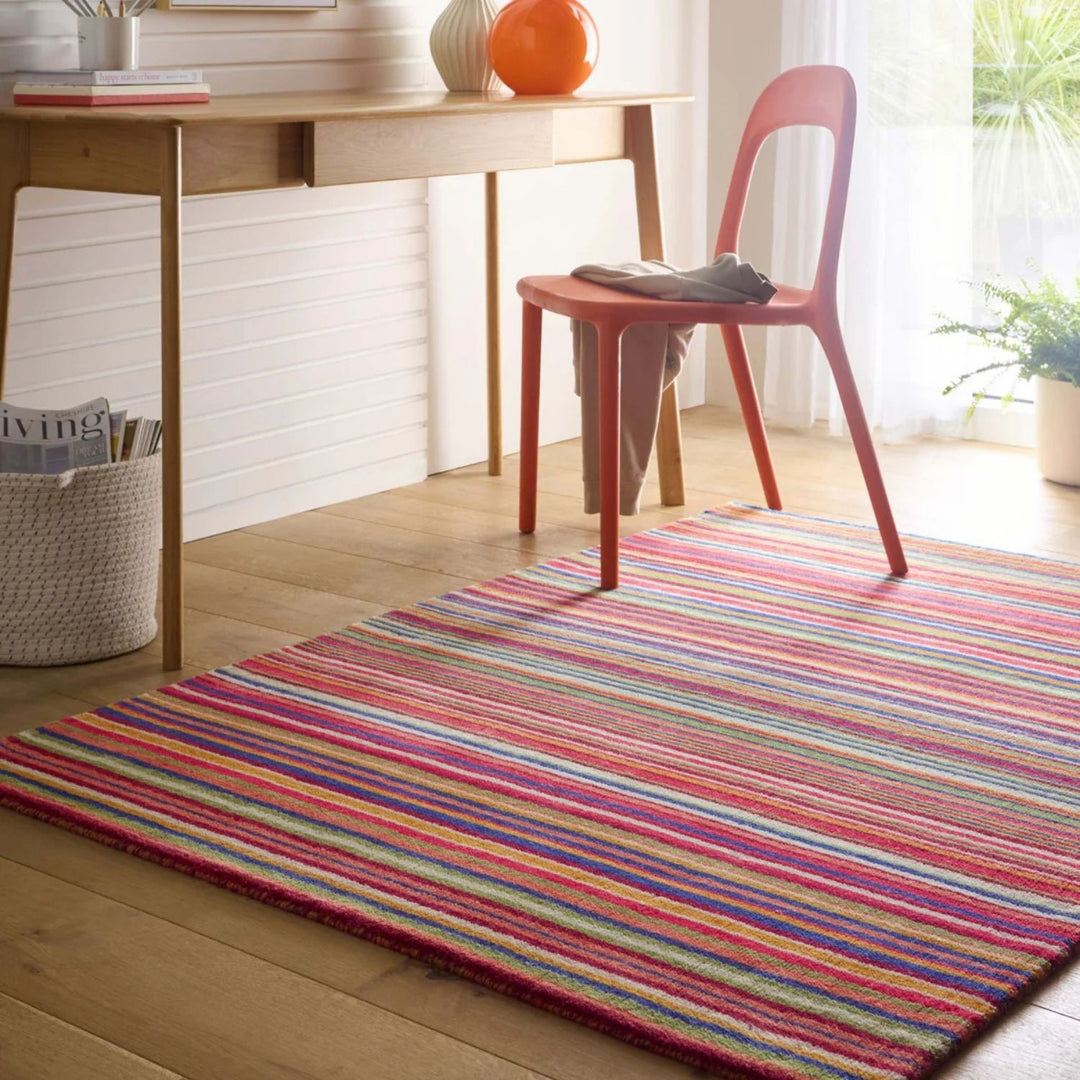 Multicolored striped rug on a wooden floor with a red chair and desk in the background.