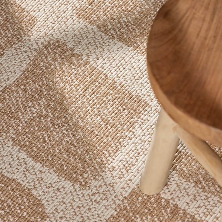 Close-up of a textured beige and brown carpet with a wooden chair leg.