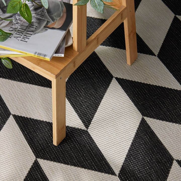 Black and white geometric patterned rug with a wooden side table and books on top.