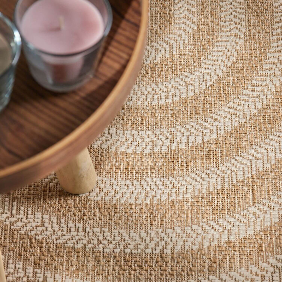 Close-up of a textured beige carpet with a wooden side table and pink candle in the background.