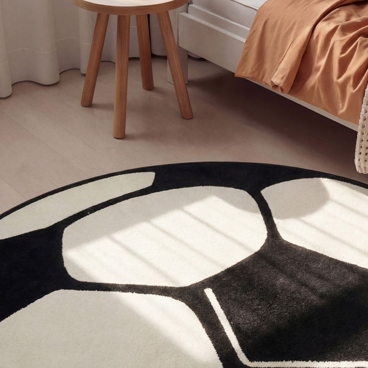 Black and white abstract rug on a wooden floor with a chair and bed in the background.