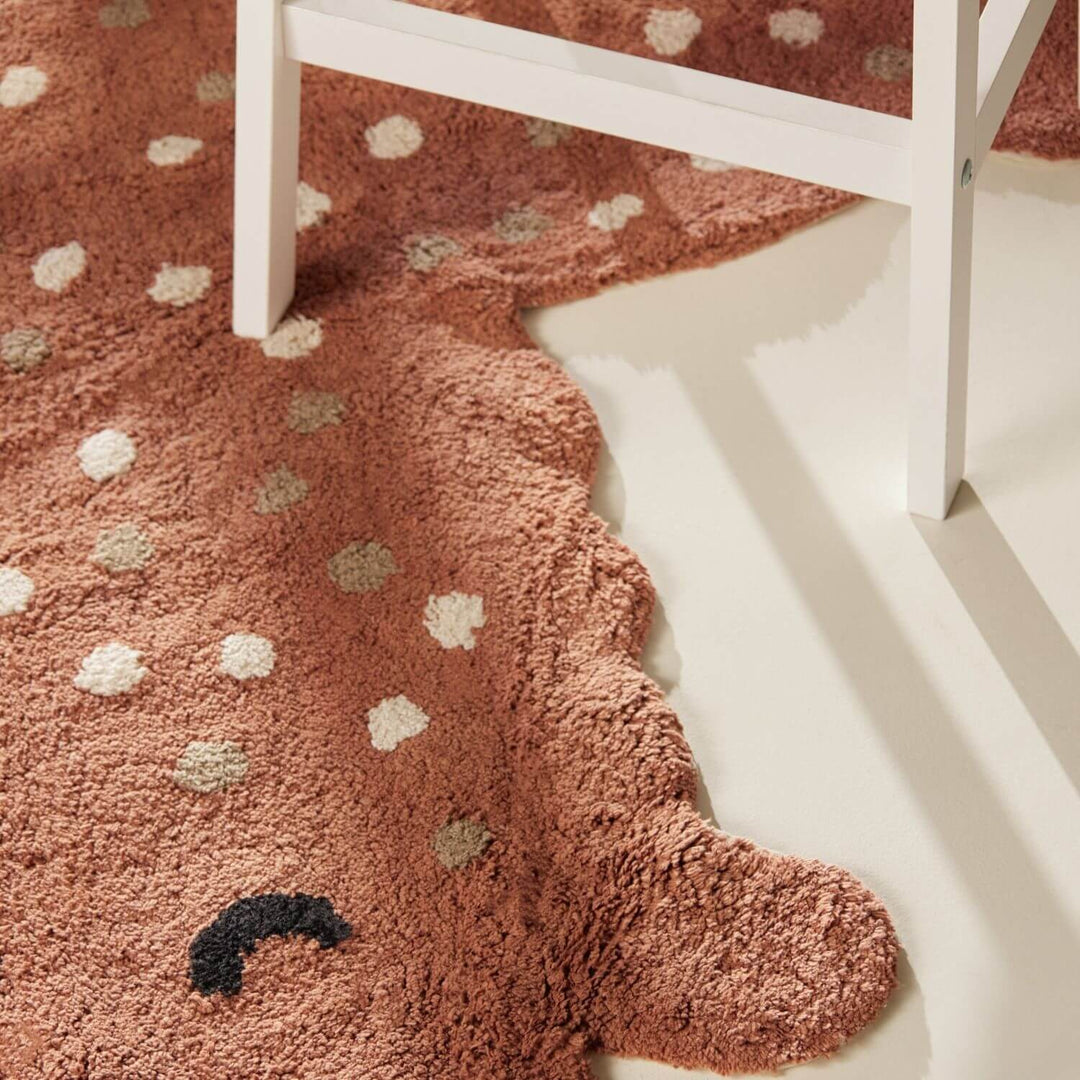 Brown rug with white and beige polka dots on a white floor.