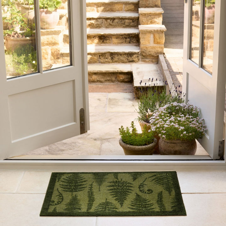 Green doormat with fern pattern in front of a glass door leading to a stone staircase.