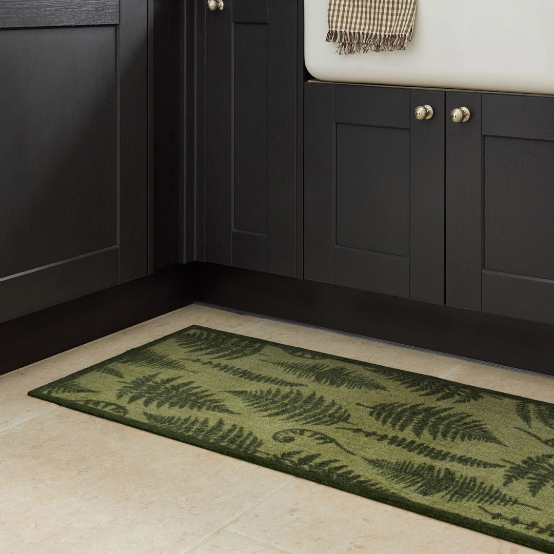 Green fern-patterned rug on a beige floor in front of dark wooden cabinets.