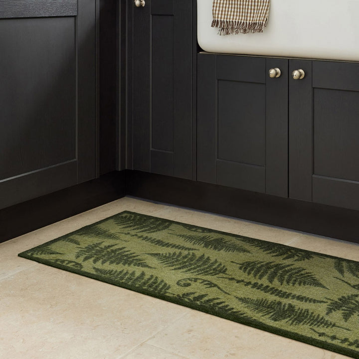 Green fern-patterned rug on a beige floor in front of dark wooden cabinets.