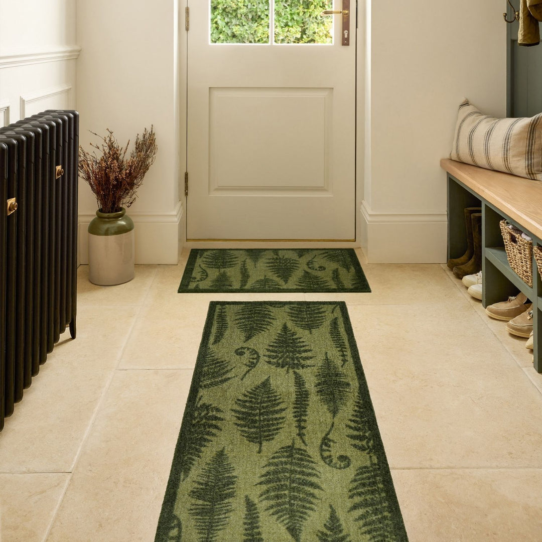 Fern patterned rug on a tiled floor with a bench and decorative items in the background.