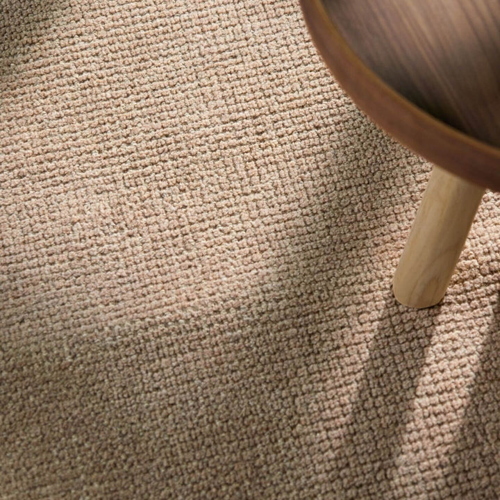 Close-up of a textured beige carpet with a wooden leg partially visible