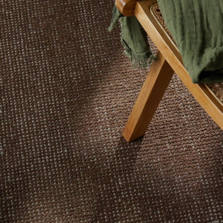 Brown textured carpet with a wooden chair and green fabric.