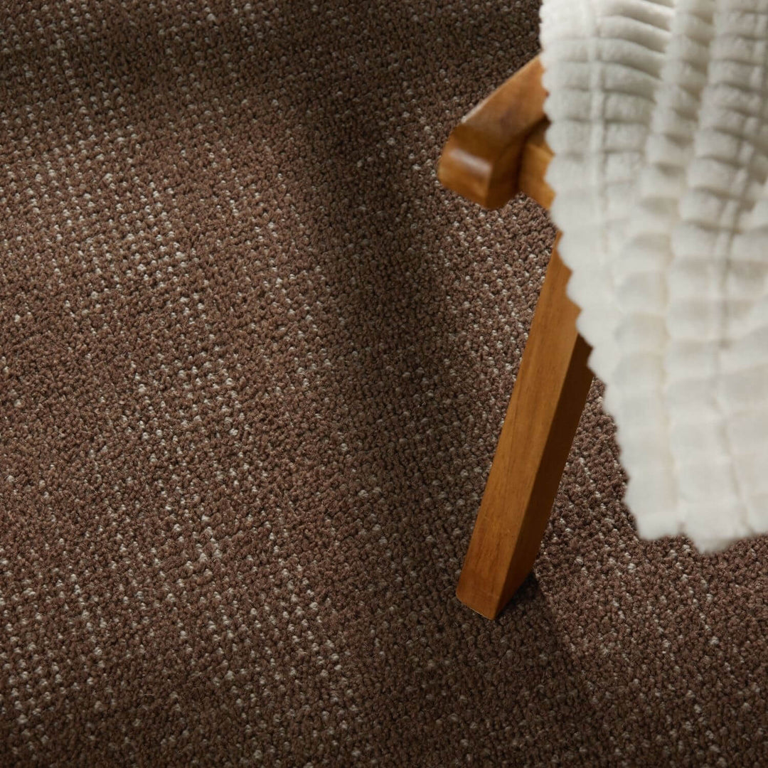 Brown textured carpet with a wooden chair leg and white fabric edge.