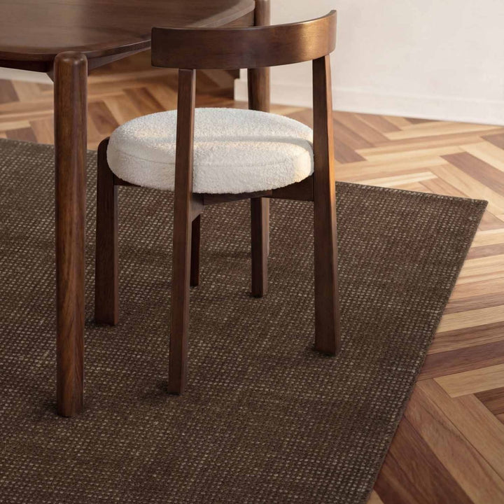 Wooden chair with a white cushion on a brown rug in a room with wooden flooring.