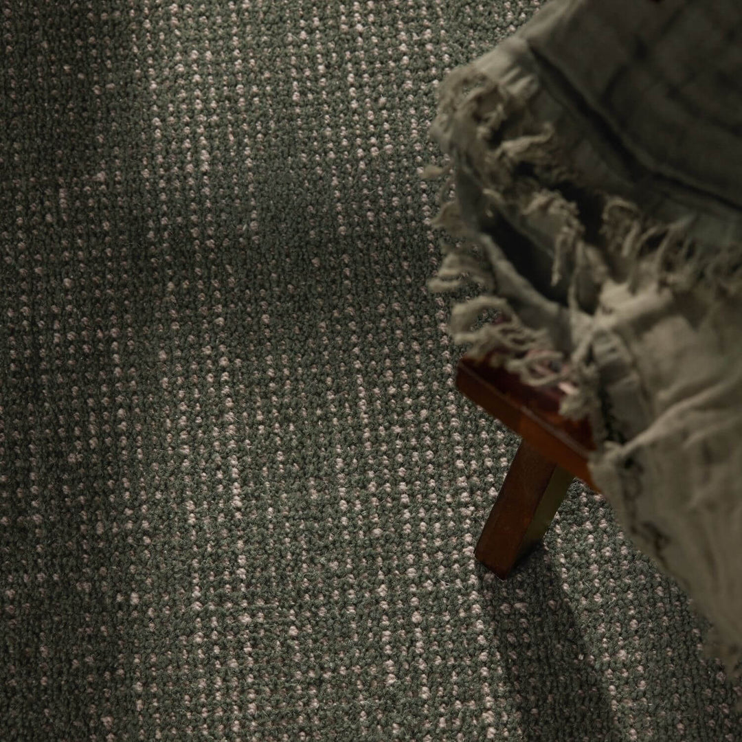 Textured green carpet with a wooden stool and a blanket on it
