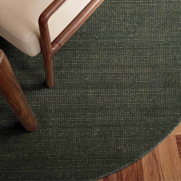 Round dark green rug on a wooden floor with a chair corner.