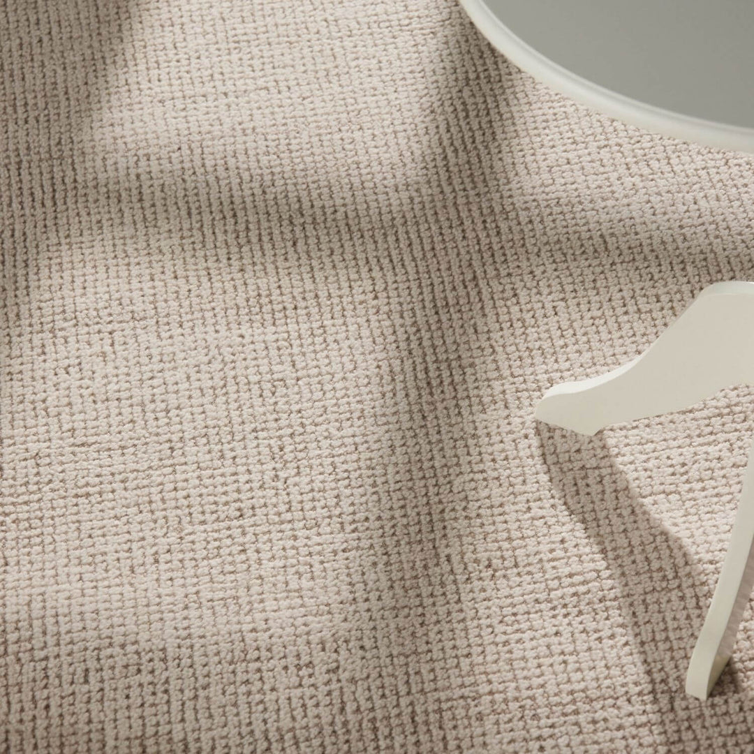 Textured beige fabric with a small white decorative item on a neutral background