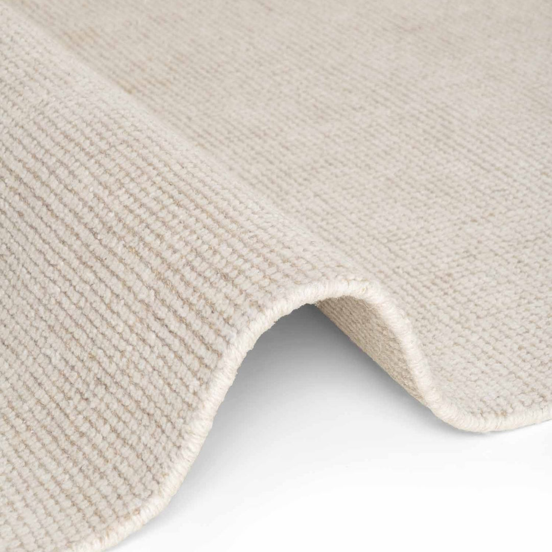 Close-up of a textured beige rug corner on a light gray background