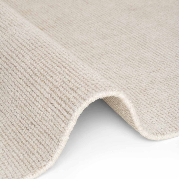 Close-up of a textured beige rug corner on a light gray background