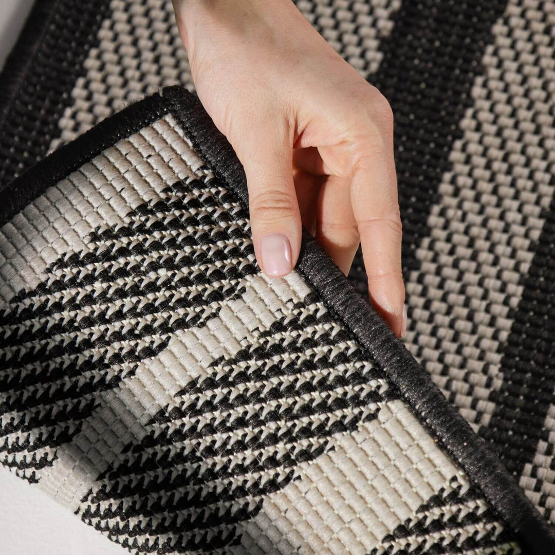 Hand holding a corner of a black and beige patterned rug