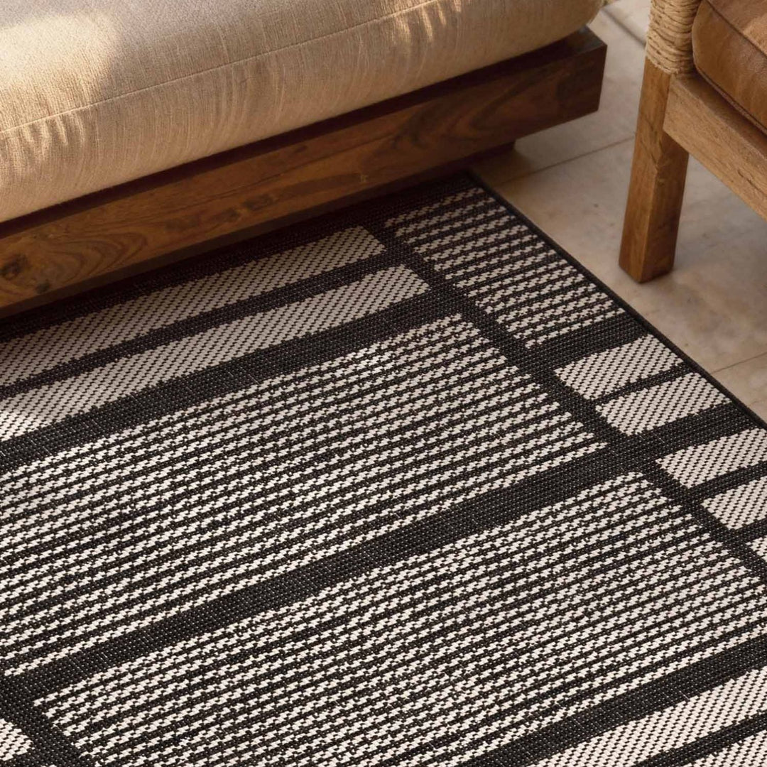 Black and white striped rug on a wooden floor with a beige sofa and wooden chair.