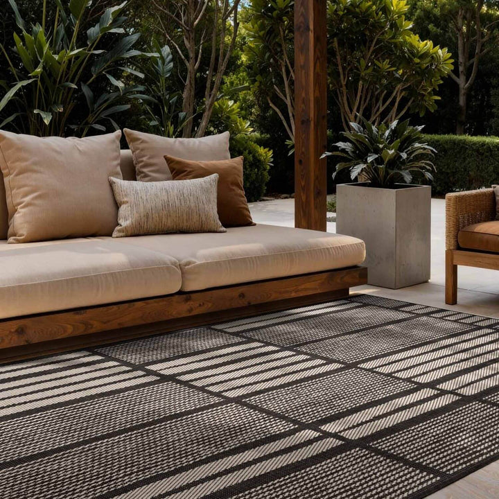 Outdoor seating area with a beige cushioned sofa and striped rug on a patio.