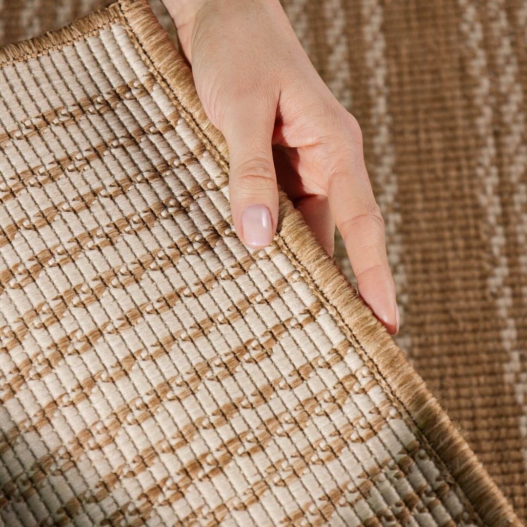 Close-up of a hand touching a textured brown and beige rug