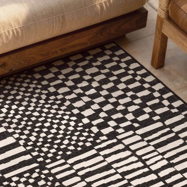 Black and white geometric patterned rug on a wooden floor with furniture.