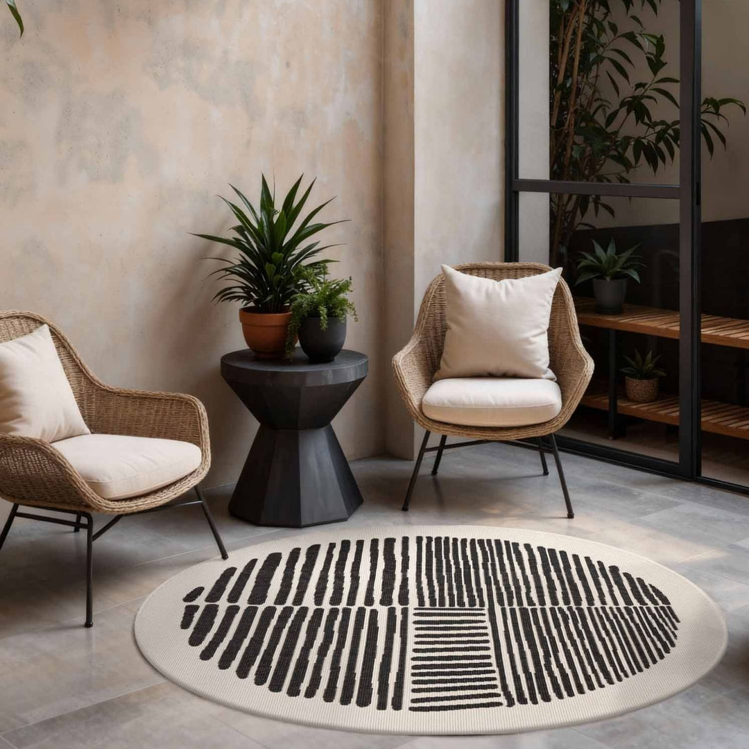 Round black and white patterned rug in a living room with wicker chairs and plants.