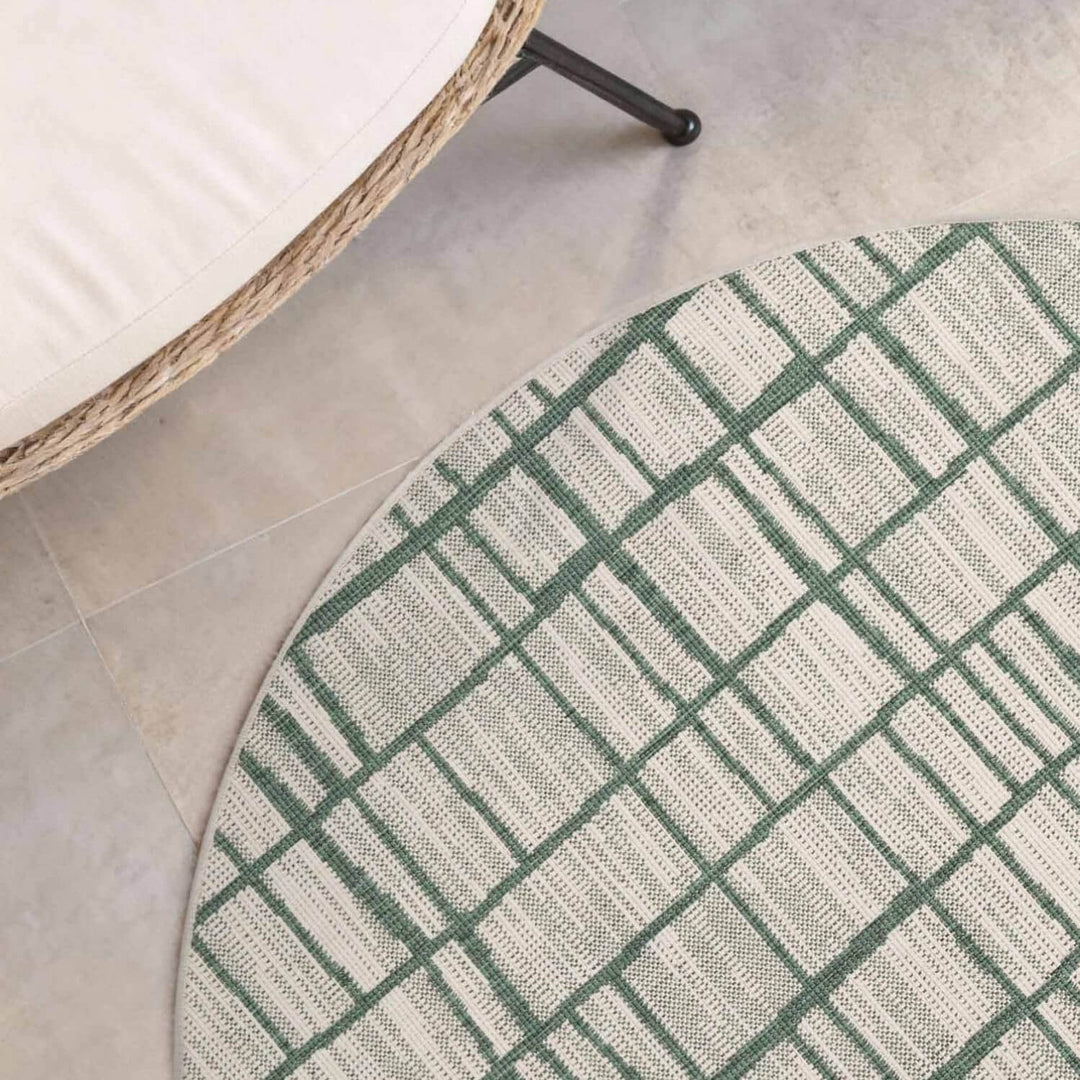 Round green and white checkered rug on a tiled floor with a wicker chair.