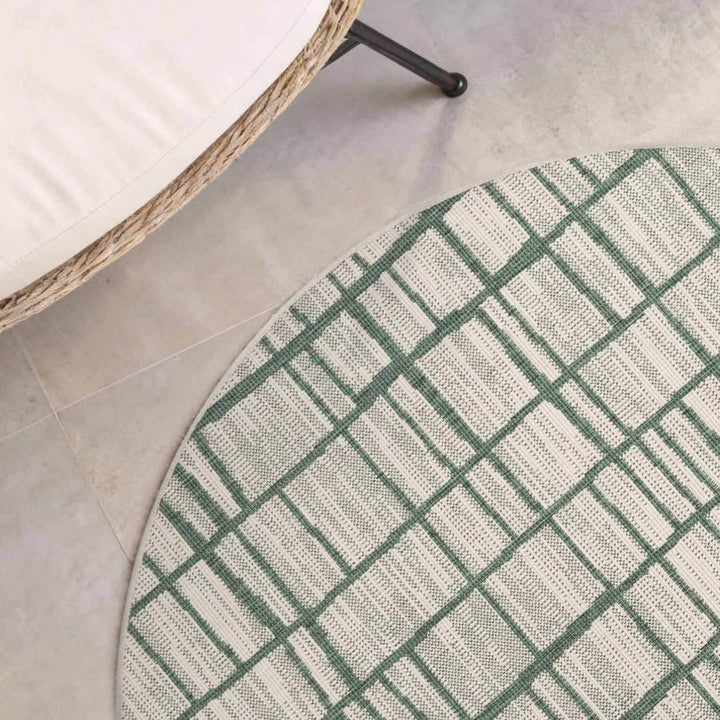 Round green and white checkered rug on a tiled floor with a wicker chair.