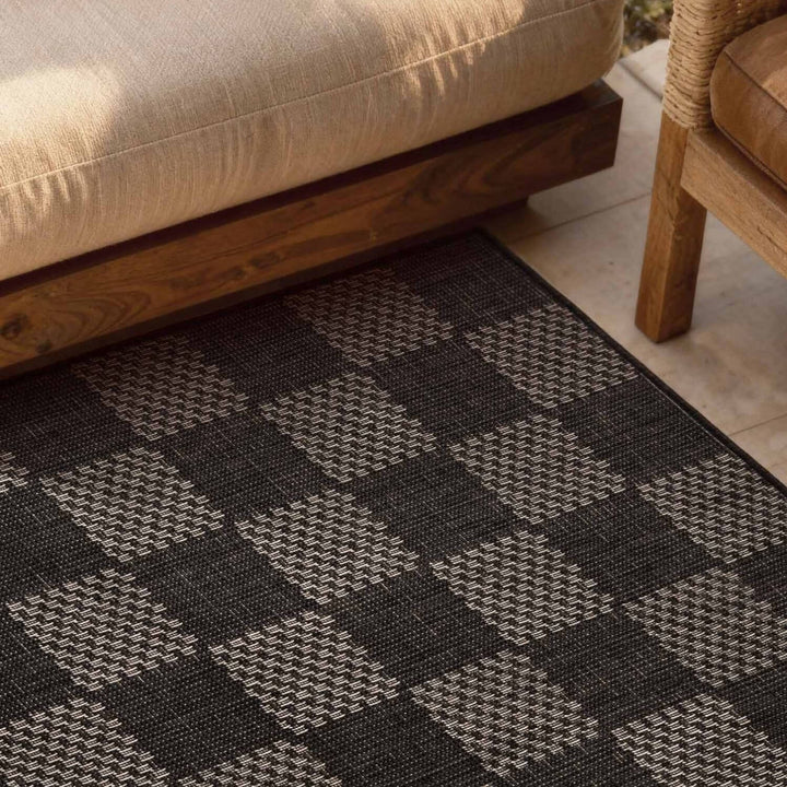 Patterned black and gray rug on a patio with wooden furniture.