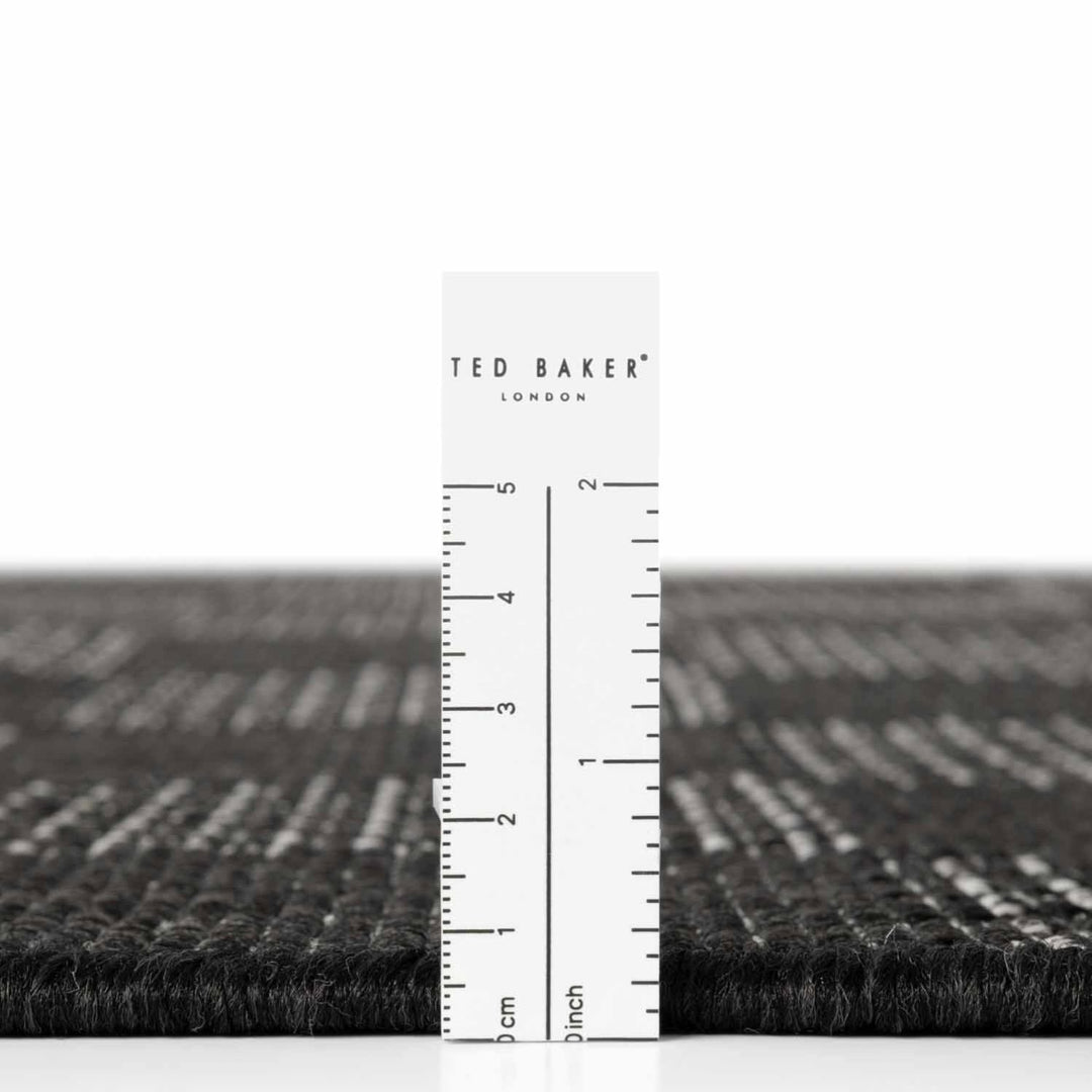 Black textured rug with a ruler for scale on a white background, featuring the Ted Baker London brand.