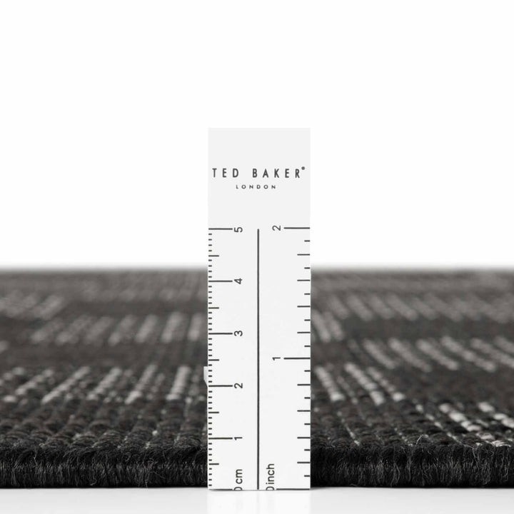 Black textured rug with a ruler for scale on a white background, featuring the Ted Baker London brand.