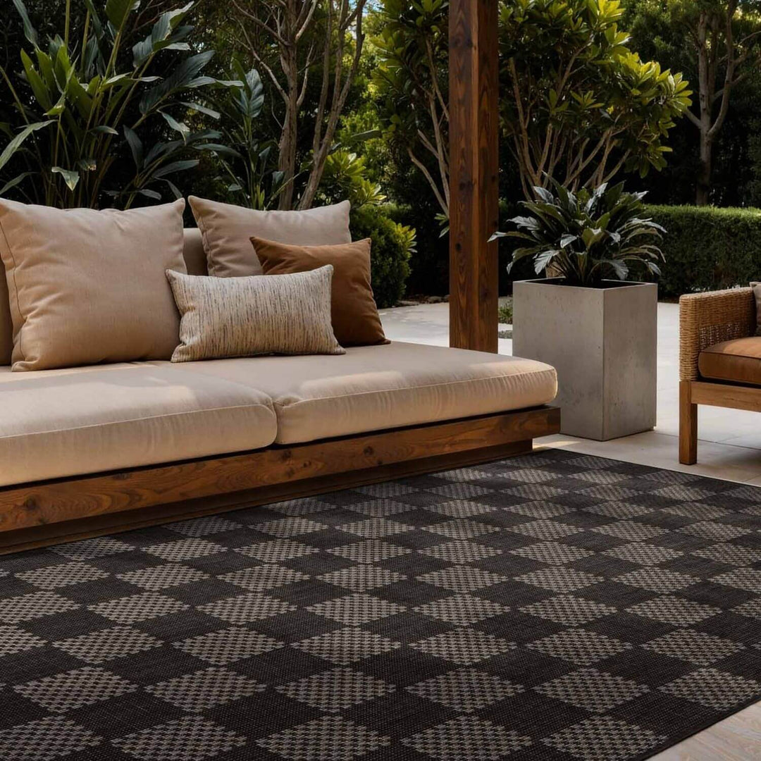 Outdoor seating area with a beige sofa, cushions, and a patterned rug.