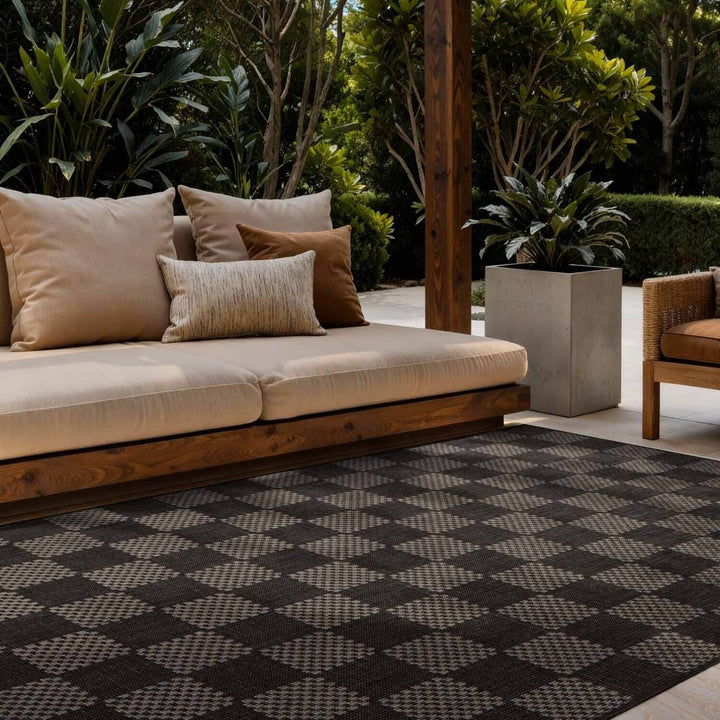 Outdoor seating area with a beige sofa, cushions, and a patterned rug.
