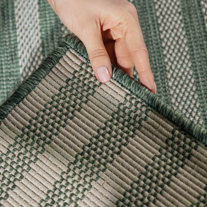Hand touching a green and beige woven rug