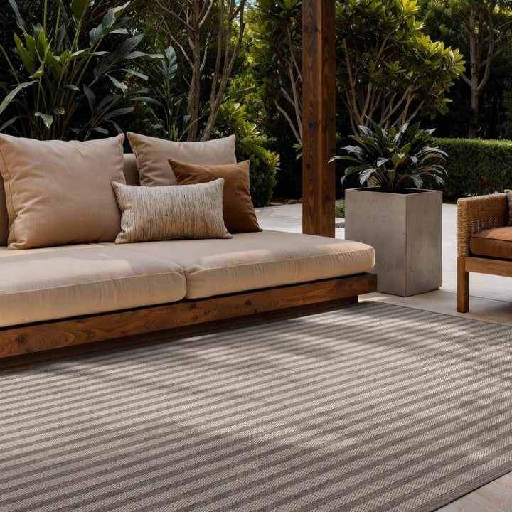 Outdoor seating area with a striped rug, cushions, and plants.