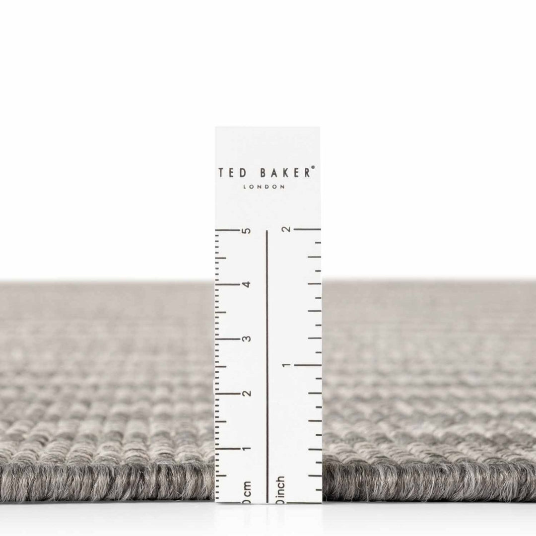 Gray textured rug with a ruler and 'Ted Baker' branding on a white background