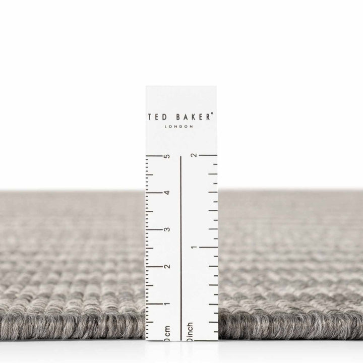 Gray textured rug with a ruler and 'Ted Baker' branding on a white background