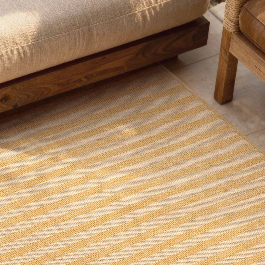 Striped yellow and beige rug on a wooden floor with a wooden chair and sofa.