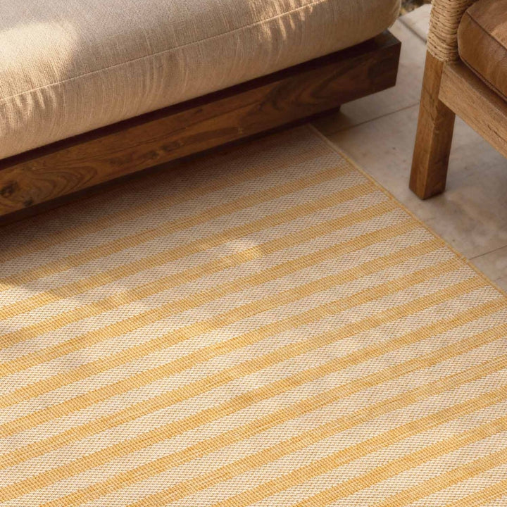 Striped yellow and beige rug on a wooden floor with a wooden chair and sofa.