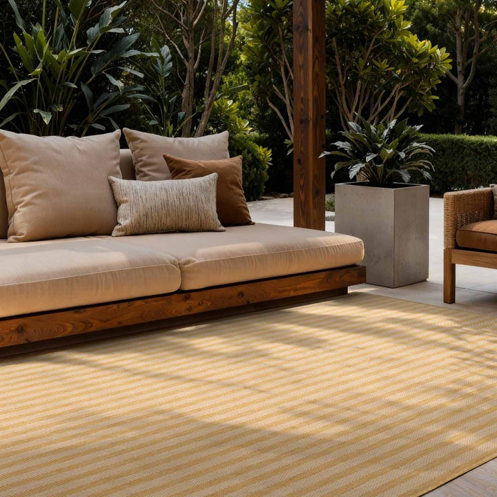 Outdoor seating area with a beige sofa, cushions, and a yellow striped rug.