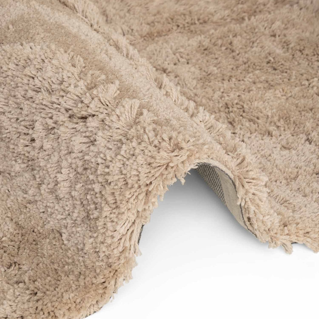 Close-up of a beige shaggy rug corner on a white background