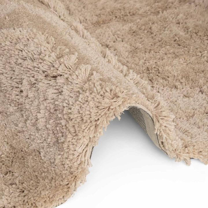 Close-up of a beige shaggy rug corner on a white background