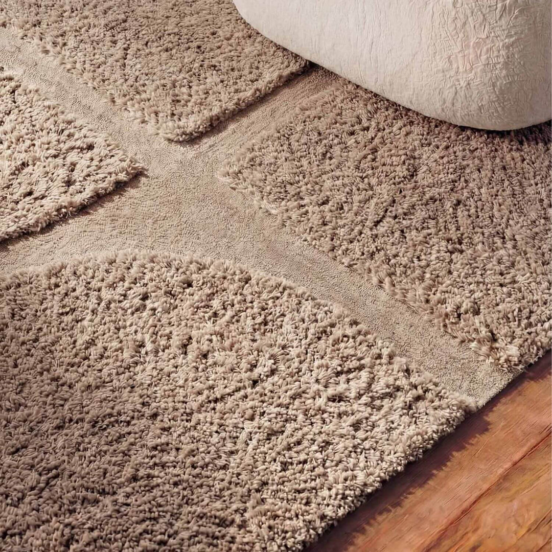 Close-up of a beige carpet being rolled out on a wooden floor.