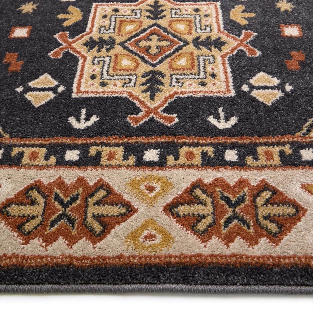 Close-up of a patterned rug with geometric designs in red, brown, and beige on a dark background.