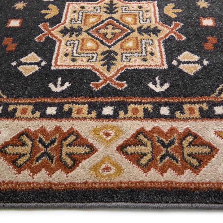 Close-up of a patterned rug with geometric designs in red, brown, and beige on a dark background.
