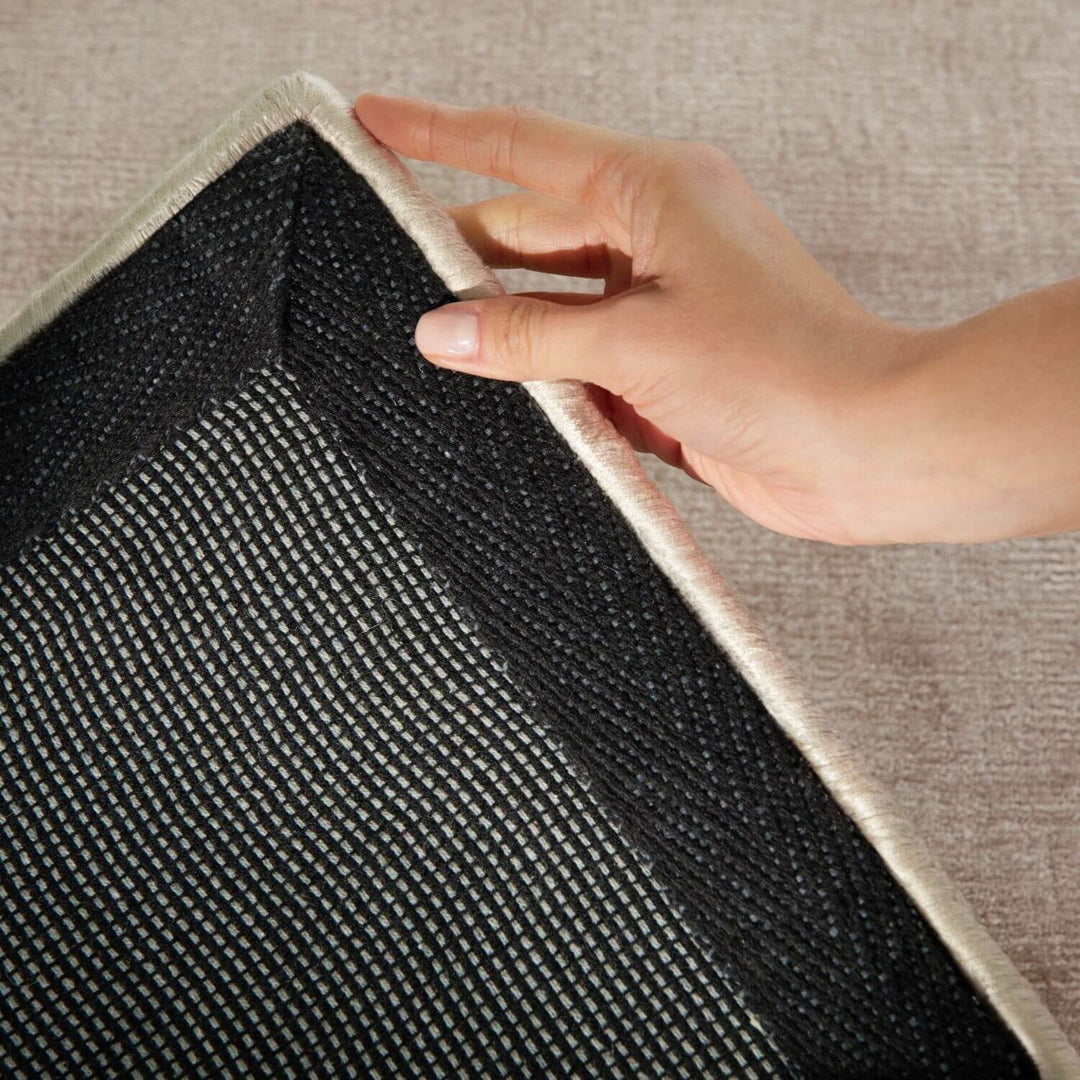 Hand pulling a rug off the floor with a textured surface.